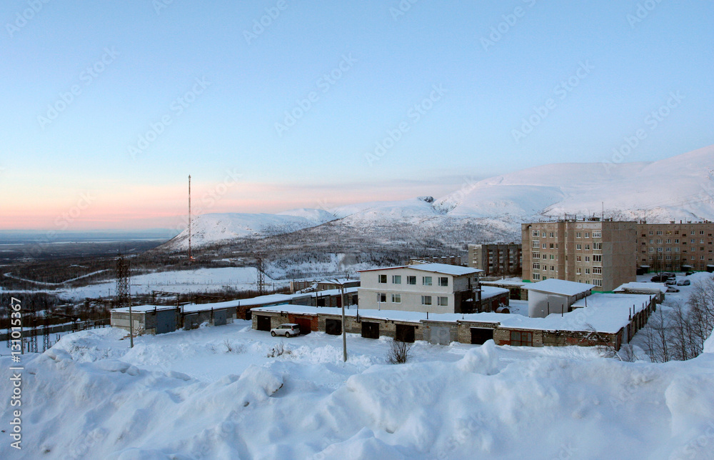 The winter evening landscape with the Russian city and snow mountains. This photo was taken in Kirovsk in Khibiny mountains, Murmansk Region, Russia. 