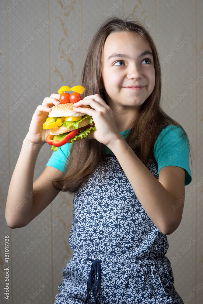 Φωτογραφία 11 year old girl with a hamburger in hand looking up with the question of whether to eat junk food