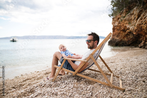 Man with his baby son at the beach, sitting on deckchair