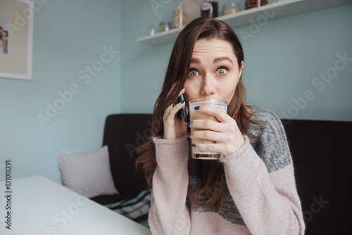 Cute shocked lady having a breakfast while talking by phone