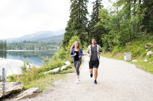 Beautiful young couple running at the lake in green nature.
