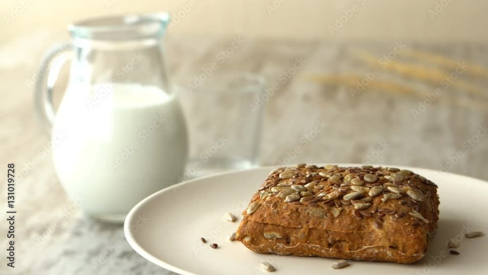 Delicious homemade small loaf of bread with seeds. Milk-jug, on wooden rustic table. Looped. Delicious homemade small loaf of bread with seeds. Milk-jug, on wooden rustic table. Looped.