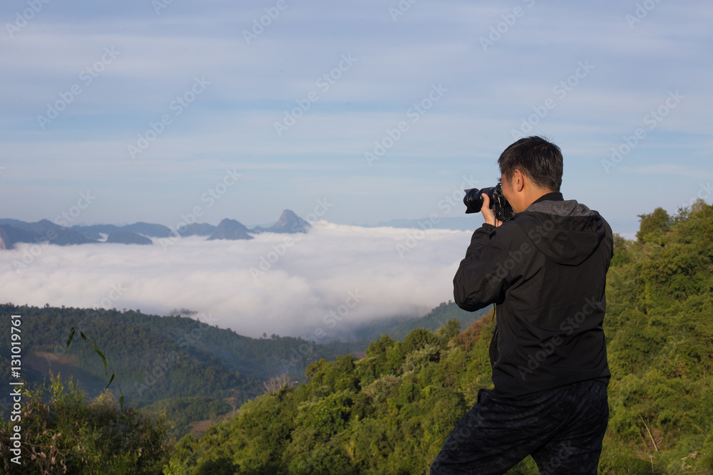 A man shooting photograph at the hill top with sea of fog and mountain view