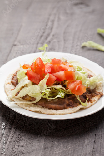Corn tortilla tostada with refried beans, lettuce, salsa, and tomatoes vertical shot
