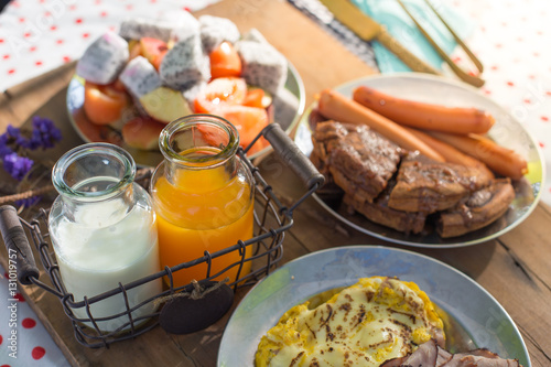 Colourful breakfast table with fruits egg and sausage, orange juice and milk 