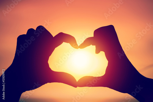 Hand making heart shape over sunset