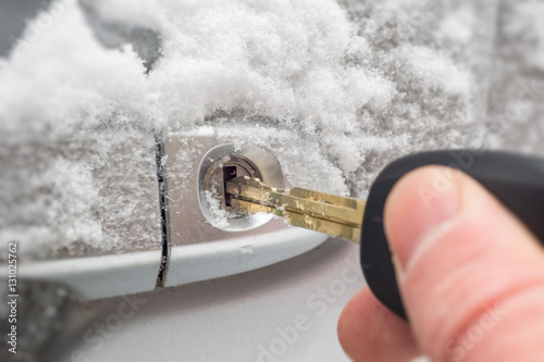 Close-up of a key inserted into the lock of frozen car door in winter © mbruxelle