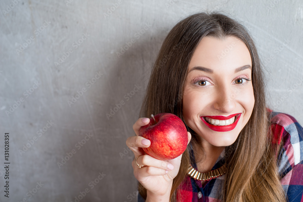 Young woman with toothy smile and red apple on the gray wall background