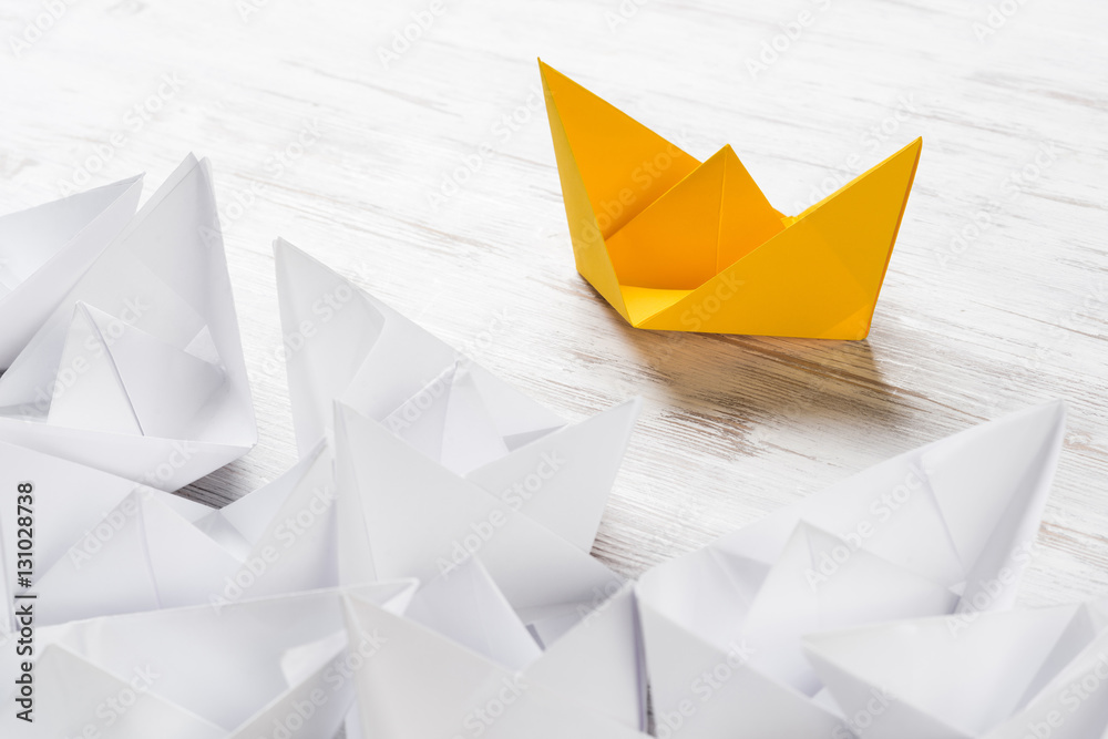 Business leadership concept with white and color paper boats on wooden table