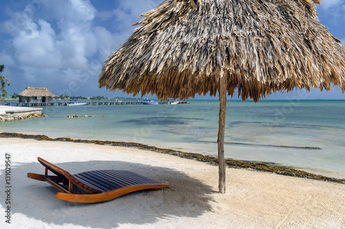 Straw beach umbrella, palapa and lounge chair on tropical beach of Ambergris Caye in Belize. photo