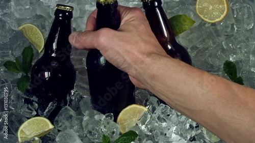 4k Shot of Cold Ice Cubes and Hand Taking Beer Bottle photo