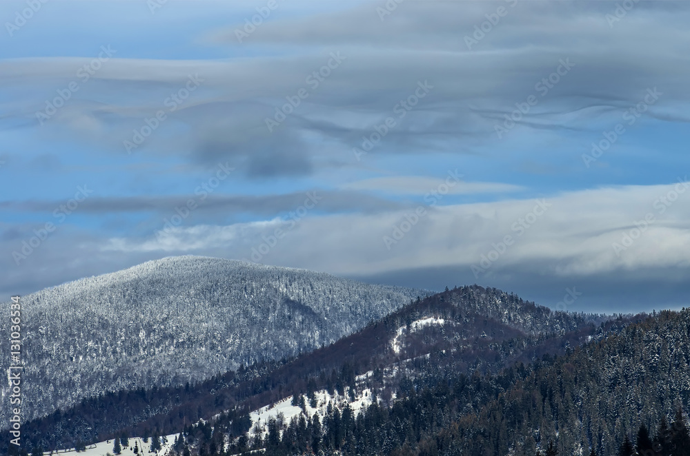 Wavy clouds over forested mountains in winter under the snow. Winter landscape. Wavy clouds over forested mountains in winter under the snow. Winter landscape.
