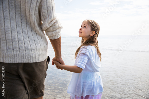 Father and daughter holding hands on a beach. Girl looks up towards father. California