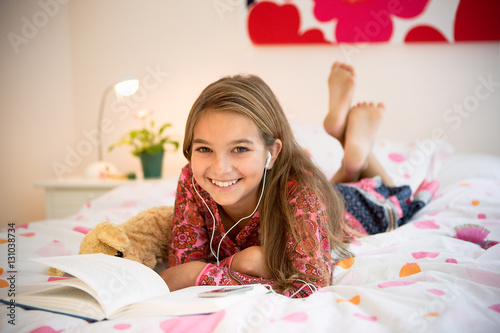 Portrait of a young girl on her bed reading and listening to music
