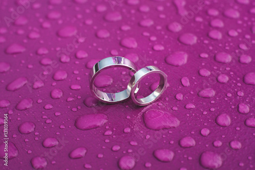 Wedding rings on a pink surface in the rain.