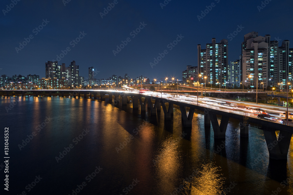 Naklejka premium Oświetlona dzielnica mieszkalna wzdłuż rzeki Han i ruch uliczny na moście w Seulu w Korei Południowej w nocy.