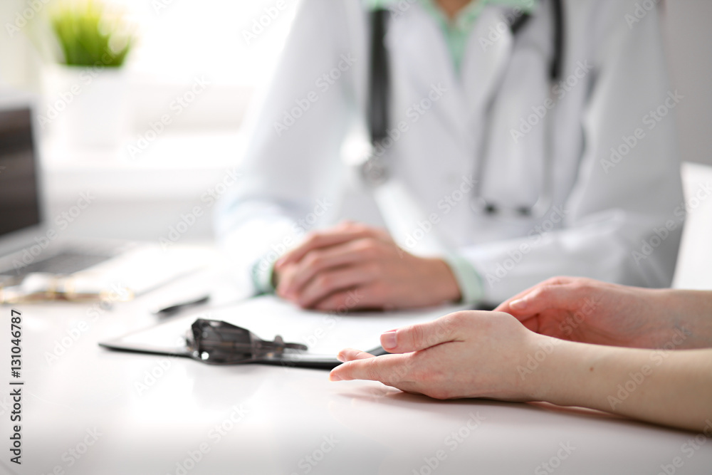 Close up of doctor and patient sitting at the desk near the window in hospital Close up of doctor and patient sitting at the desk near the window in hospital