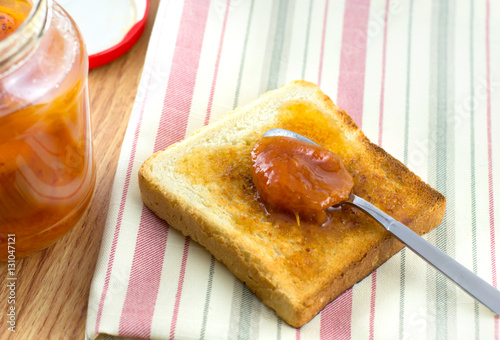 apricot jam spread on a slice of bread with jam jar on a napkin