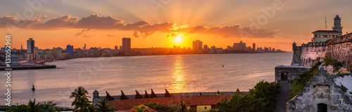 Sunset in Havana with the sun setting over the seaside buildings including a view of El Morro lighthouse © kmiragaya