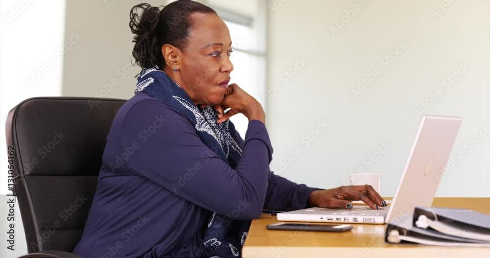 A black businesswoman uses a laptop at her desk. An African American woman thinks about her work on her computer
