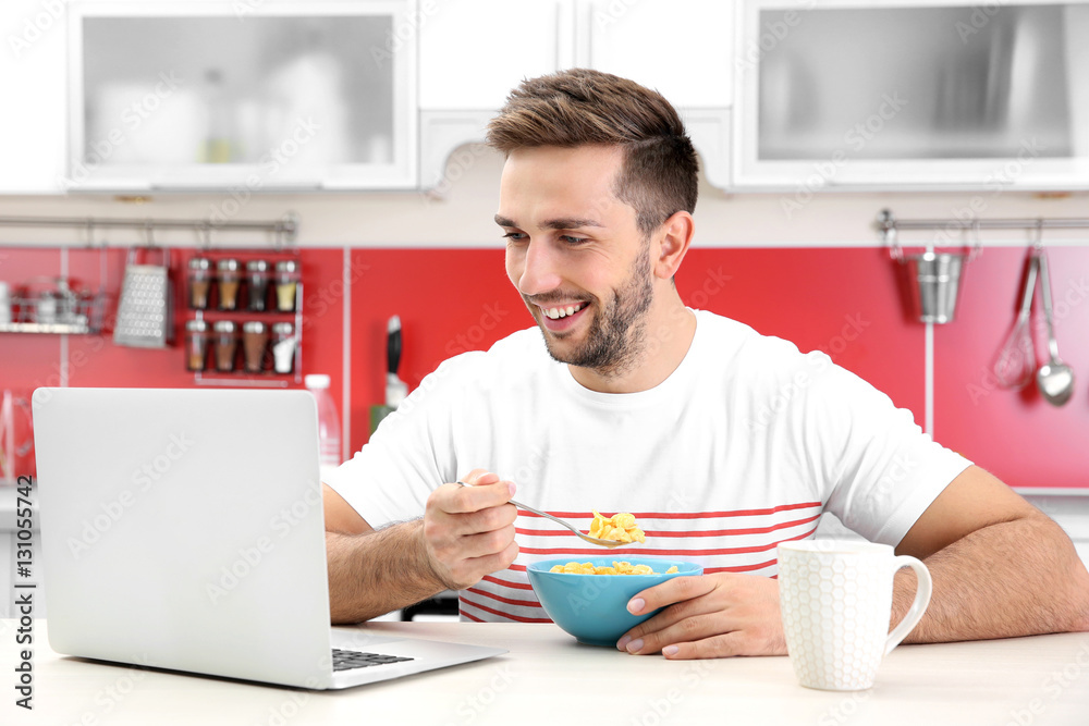 Young man having breakfast while working with laptop in kitchen Young man having breakfast while working with laptop in kitchen