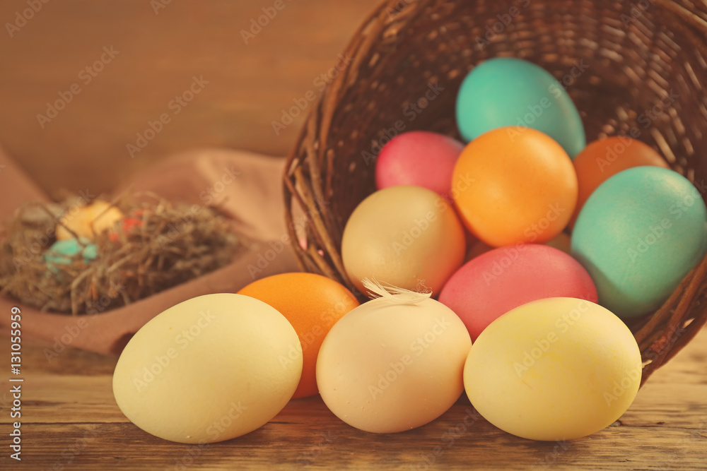 Wicker basket with colorful Easter eggs on wooden table Wicker basket with colorful Easter eggs on wooden table