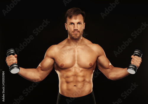 Sporty young man with dumbbells on black background © Africa Studio