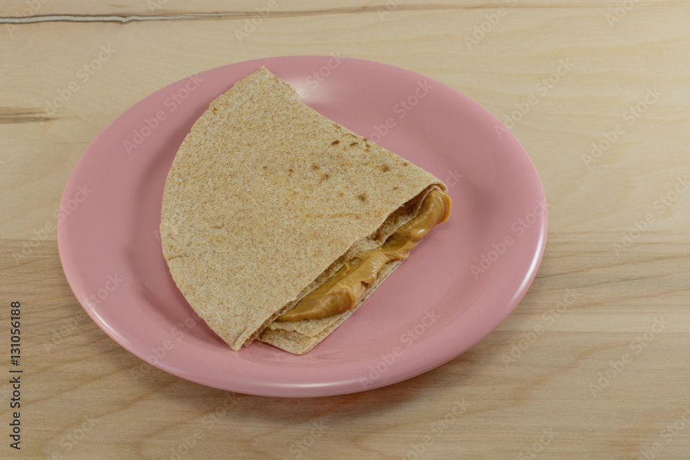 Peanut butter sandwich with whole wheat tortilla bread on pink plate Peanut butter sandwich with whole wheat tortilla bread on pink plate