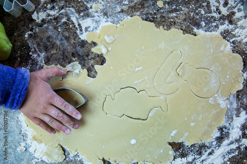 Overhead of child pressing a cookie cutter into sugar cookie dough to make Christmas cookies. photo