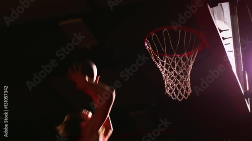 A basketball player dunks the ball, dark lighting, slow motion, view from below