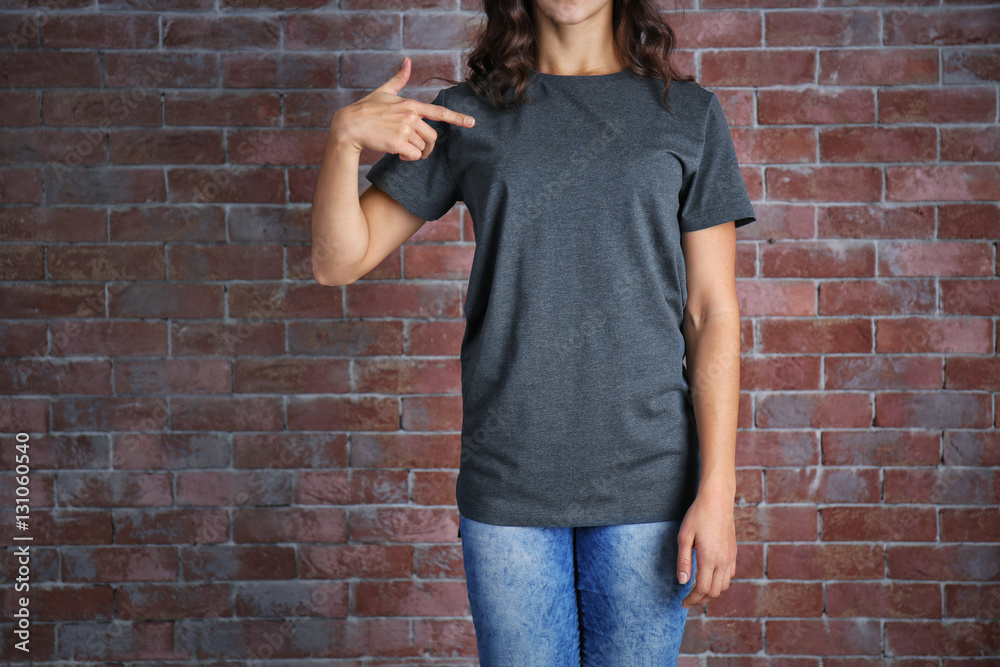 Young woman in blank grey t-shirt standing against brick wall, close up Young woman in blank grey t-shirt standing against brick wall, close up