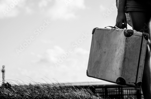 Ethnical girl standing with her old suitcase on the countryside