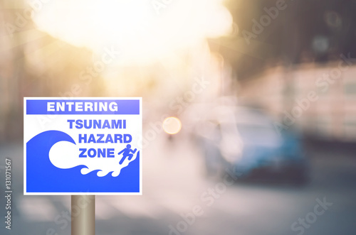 Tsunami hazard zone warning sign on blur traffic road with colorful bokeh light abstract background.