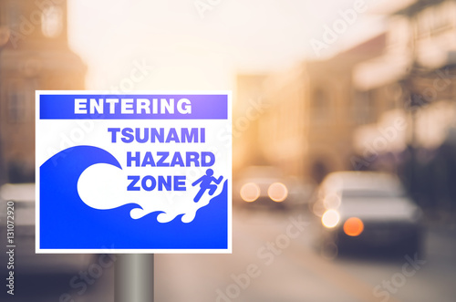 Tsunami hazard zone warning sign on blur traffic road with colorful bokeh light abstract background.