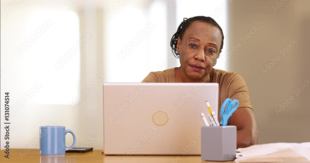 A portrait of an older black woman using her computer in her home. An elderly black woman posing for a portrait using her laptop