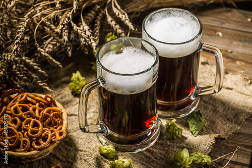 Принти на полотні Two tankard beer with wheat and hops , basket of pretzels
