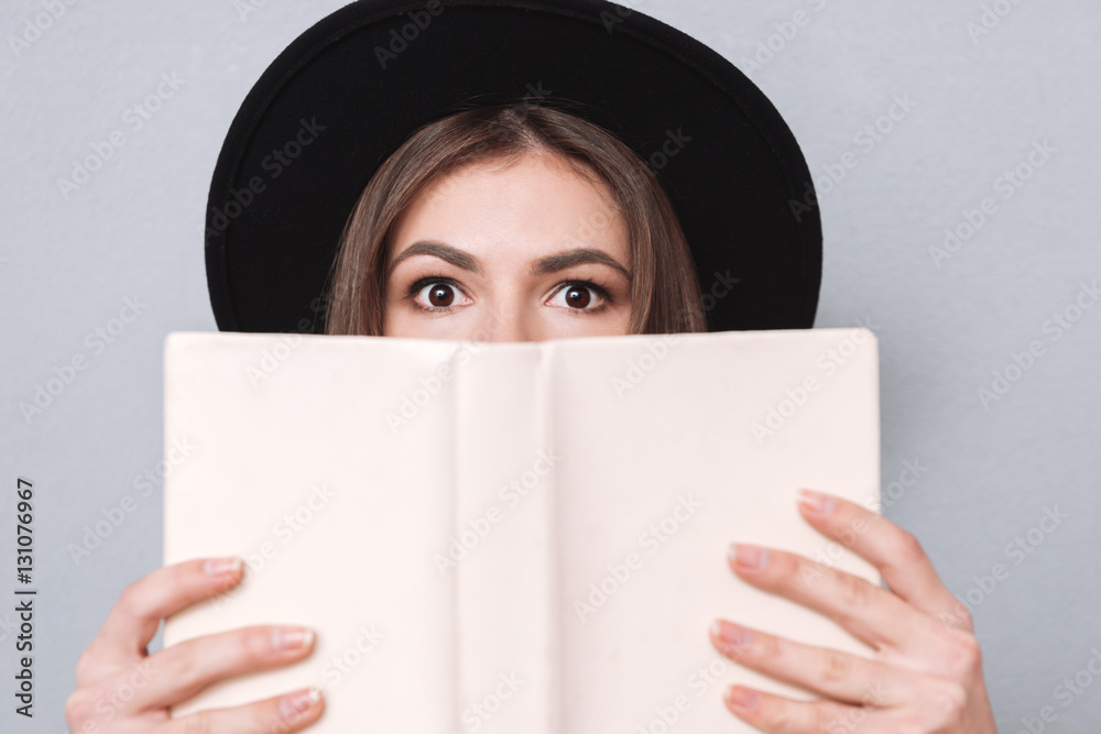 Young woman in hat covering her mouth with book Young woman in hat covering her mouth with book