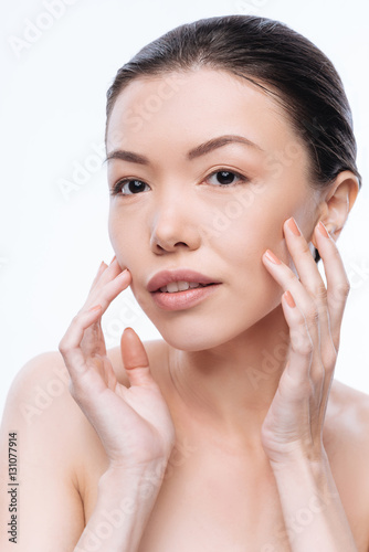 Involved young Mongolian woman touching her healthy skin