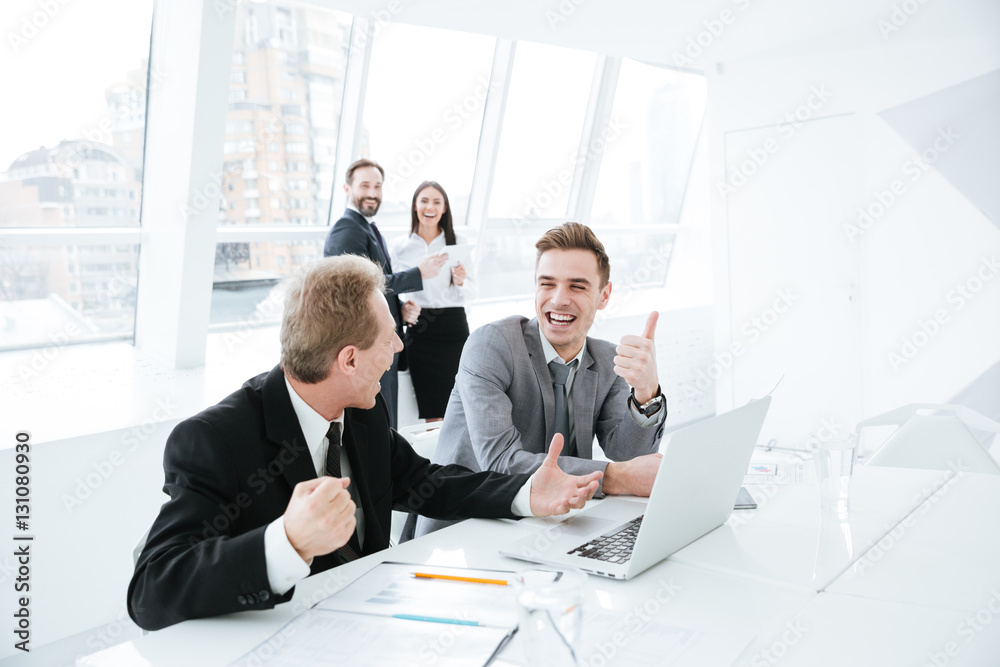Side view Business partners by table with colleagues on background Side view Business partners by table with colleagues on background
