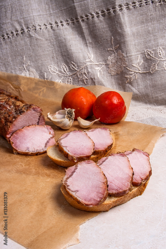 Slices smoked meat or ham on brown packing paper. Tomatoes, garl