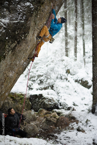 Extreme winter sport climbing. Young male rock climber on a rock wall. Snowy forest on the background, 