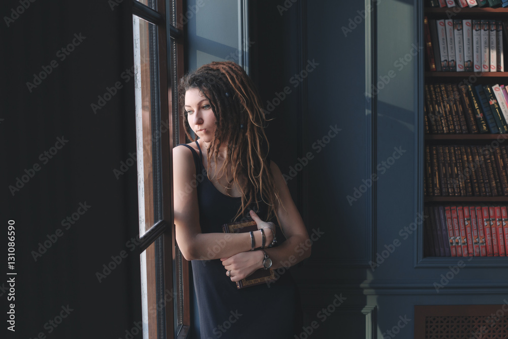 Obraz premium young girl in the library, standing the window in thought