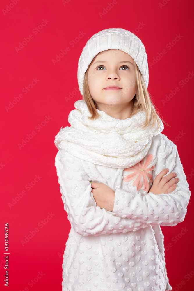 little smiling blonde girl in a white hat and scarf on red backg little smiling blonde girl in a white hat and scarf on red backg