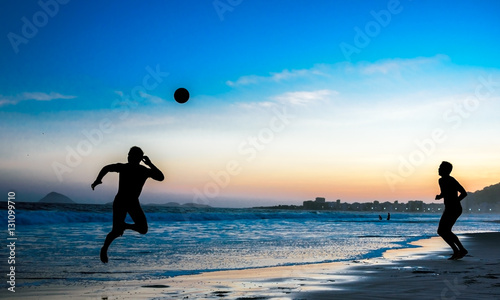 Silhouettes of two jumping men playing beach football on the background of beautiful sunset and Atlantic ocean at Copacabana beach, Rio de Janeiro, Brazil