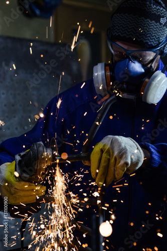 Industrial worker producing hot sparks while grinding steel metal pipe in workshop