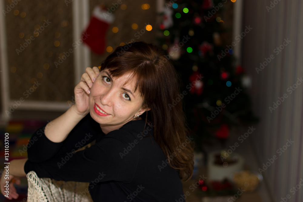 Girl sits on a background of lights Christmas tree. Christmas Ev