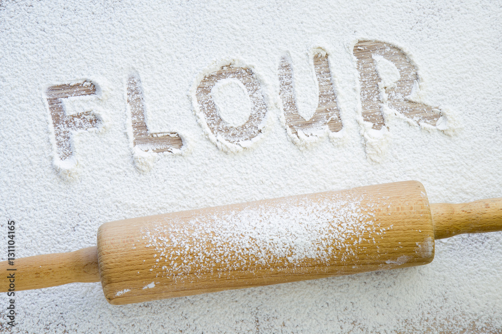 Word flour in the white flour on the wooden table in the kitchen. Rolling-pin. Word flour in the white flour on the wooden table in the kitchen. Rolling-pin.