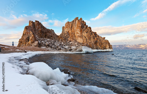 Baikal Lake in December morning. Shamanka Rock in red lichen. Icicles on the edge of the bay