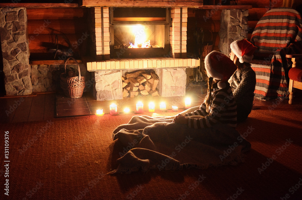 Christmas and New Year holidays, children in santa hats near fireplace in wooden house, kids have fun
