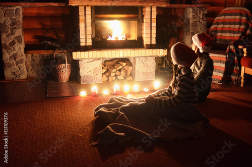 Christmas and New Year holidays, children in santa hats near fireplace in wooden house, kids have fun 